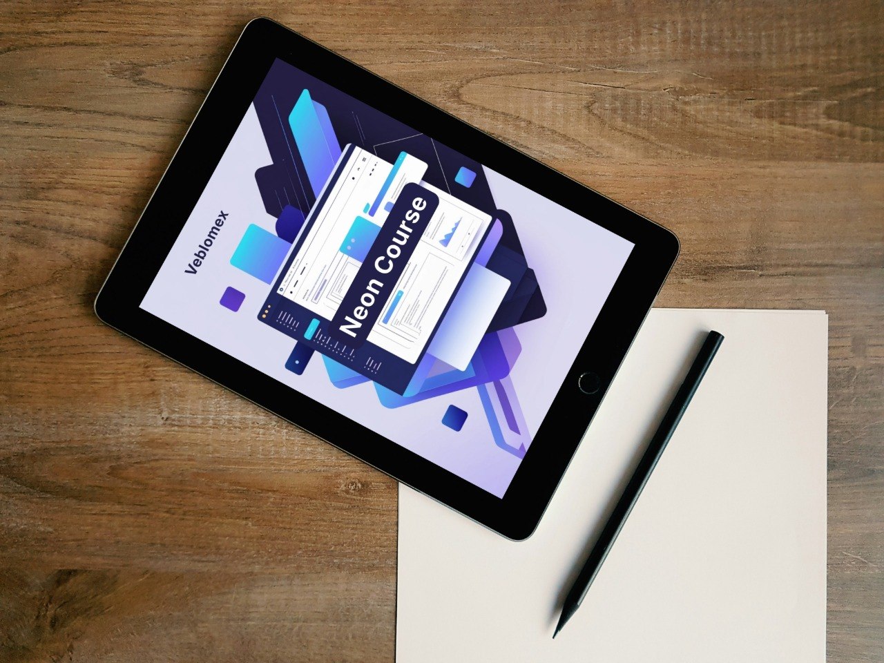 Tablet displaying a neon course design on a wooden surface with a pen and paper.